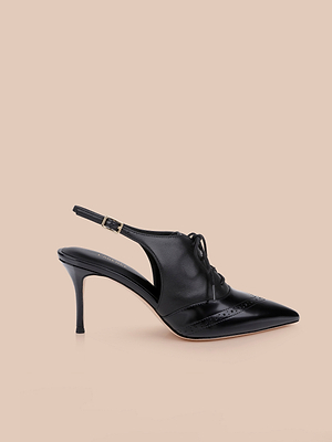 The Shreya Leather Slingback Pump, a black leather oxford stiletto with a pointed toe, lace-up front, and cutout sides, is displayed against a light beige background.