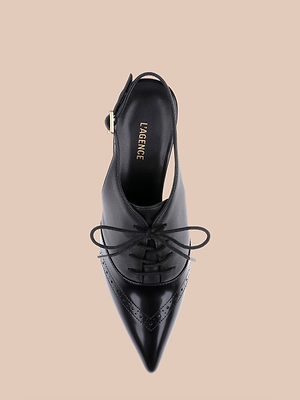 Top view of the Shreya Leather Slingback Pump, a black leather pointed-toe oxford stiletto with cutout sides and a buckle strap at the heel, shown on a plain beige background. The insole displays the L’AGENCE brand name in gold letters.