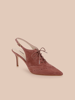 The Shreya Suede Slingback Pump, featuring a mauve suede upper, pointed toe, lace-up front, perforated details, and a small buckle strap, is displayed against a pale pink background.