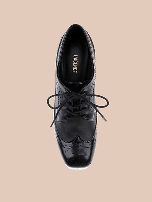 The Tania Oxford Pump is a black leather wingtip oxford with laces, seen from above on a beige background. Its insole features LAGENCE in gold lettering.