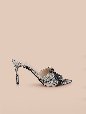 The Thames Sandal is a high-heeled mule featuring a black and white marbled pattern, stiletto heel, open toe, and a small black bow on the upper, shown against a plain light beige background.