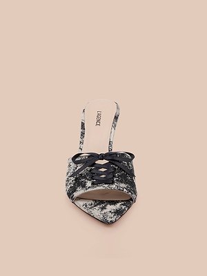 The Thames Sandal is a pointed-toe lace-up mule with a black-and-white marbled pattern, stiletto heel, black laces, and light beige insole branded Loeffler. Set against a solid nude background.
