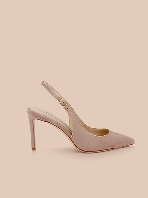 The Vichy Slingback Pump is a tan suede stiletto with a pointed toe, adjustable ankle strap, and gold piping, shown on a light peach background.