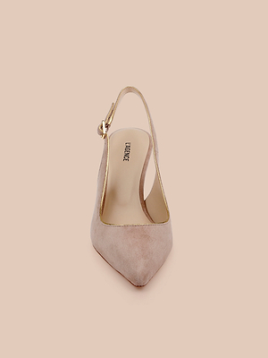 The Vichy Slingback Pump, a tan suede stiletto with a pointed toe, gold piping, and an ankle strap, is photographed from the front against a light peach background.