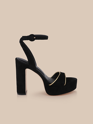 The Essie Platform Sandal features black suede, a thick heel, ankle strap, and gold trim on the front strap, shown against a beige background.