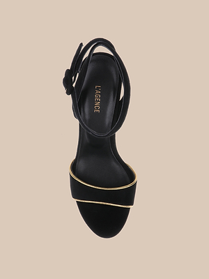 The Essie Platform Sandal is a black suede heeled sandal with an open toe, wide single strap, thin gold accent, ankle strap, and LAGENCE branding on the insole, shown against a beige background.
