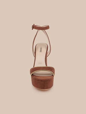 Front view of the Essie Platform Sandal in brown, featuring an ankle strap and gold piping on the toe strap, shown against a beige background.