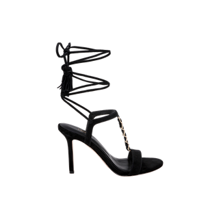 The Bond Suede Sandal features a black high heel, a single toe strap, elegant gold chain detail along the T-strap, and black ankle wrap laces tied in a bow at the back—showcasing its sophisticated strappy silhouette.
