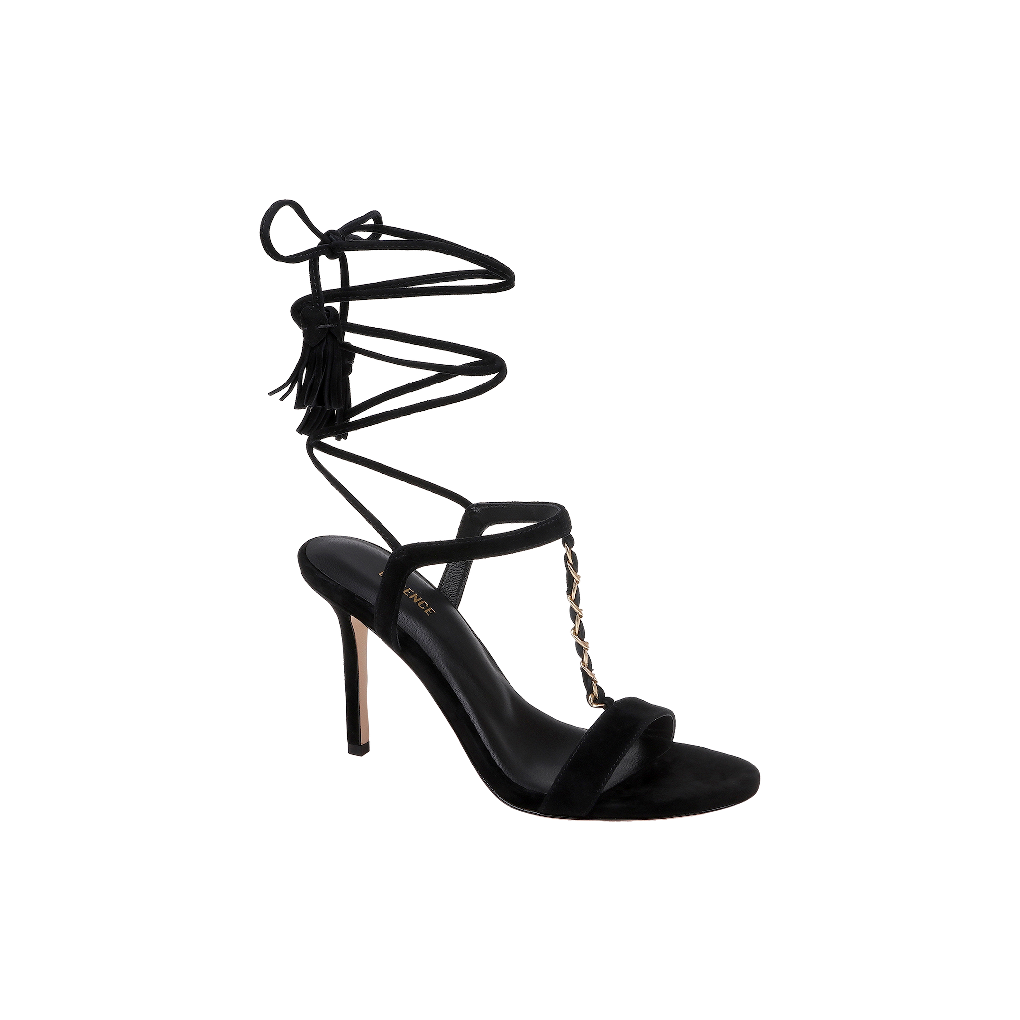 The Bond Suede Sandal is a black high-heeled shoe with a strappy design, featuring an open toe, stiletto heel, gold chain detail on the front, and a thin ankle wrap strap that ties around the ankle with tassel accents.