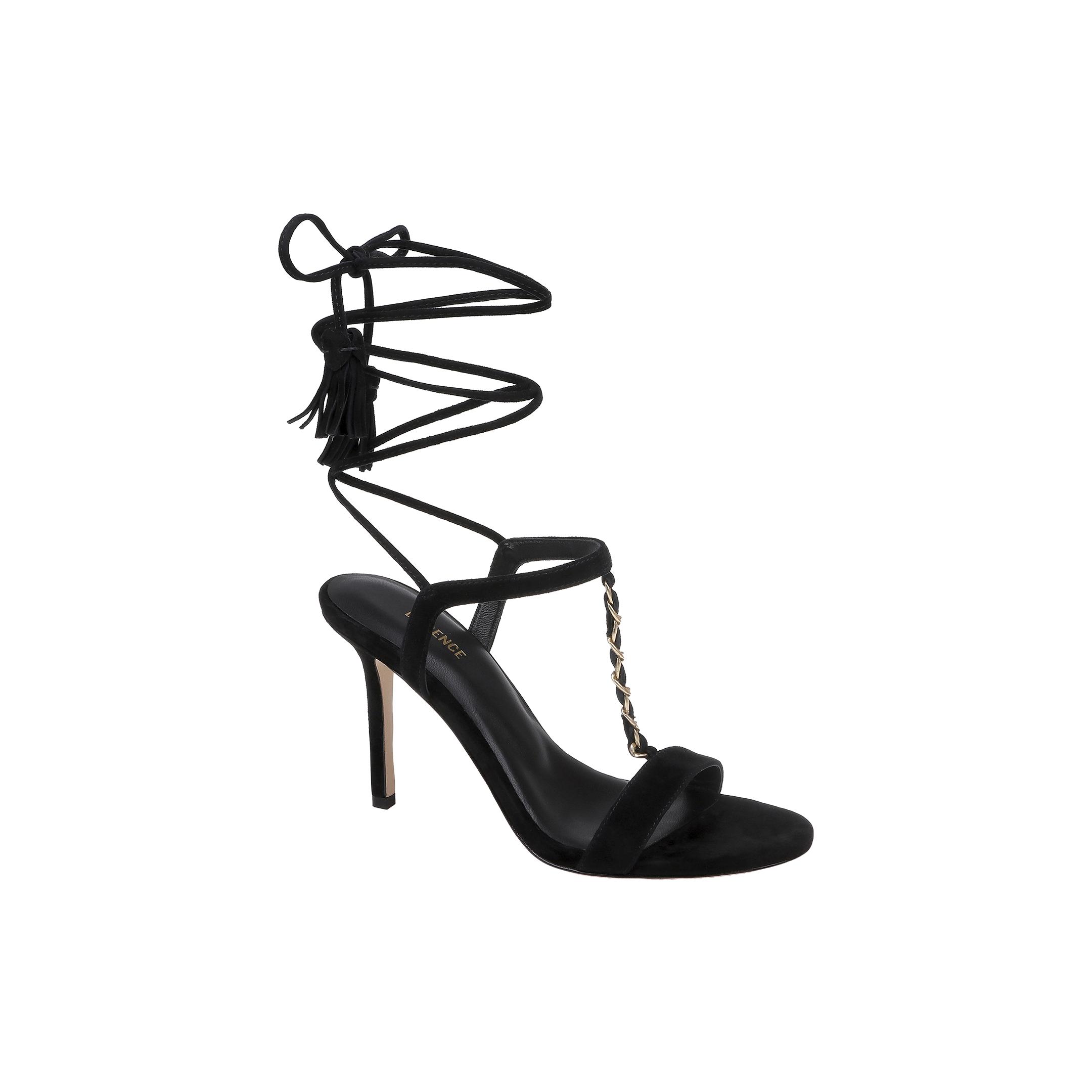 The Bond Suede Sandal is a black high-heeled shoe with a strappy design, featuring an open toe, stiletto heel, gold chain detail on the front, and a thin ankle wrap strap that ties around the ankle with tassel accents.
