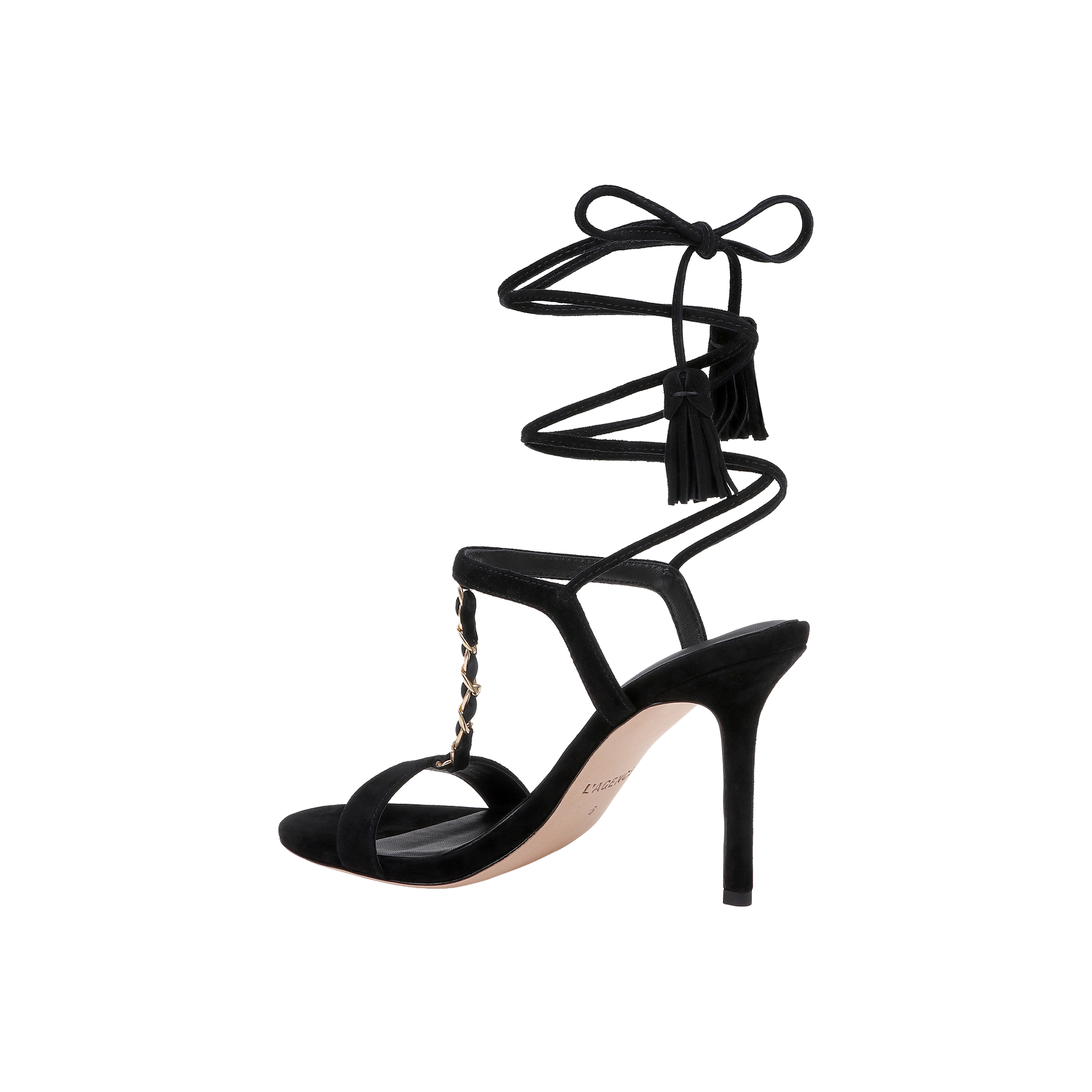 The Bond Suede Sandal is a black high-heeled shoe featuring an open toe, ankle wrap-around laces with tassel details, and a gold chain accent on the upper strappy heel.