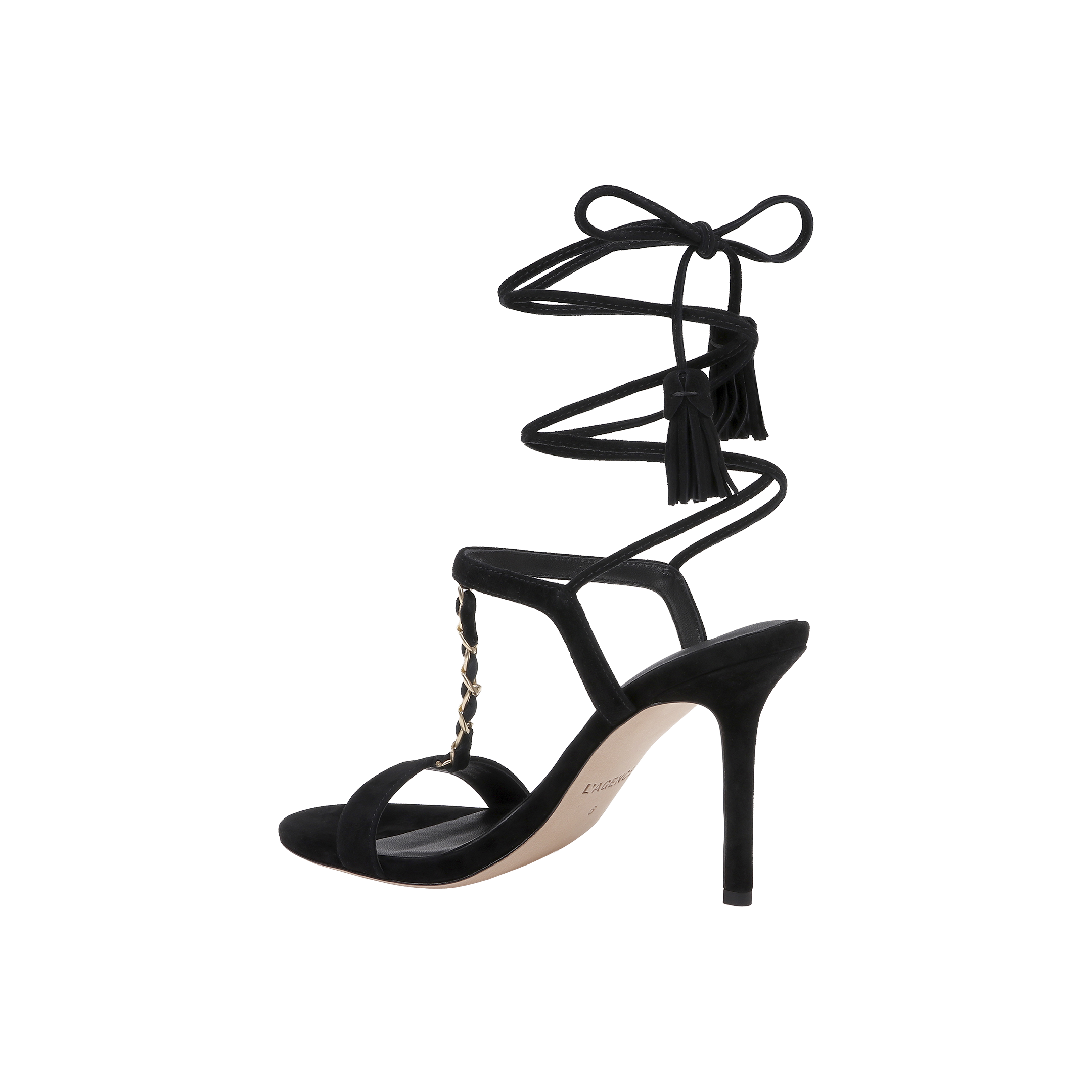 The Bond Suede Sandal is a black high-heeled shoe featuring an open toe, ankle wrap-around laces with tassel details, and a gold chain accent on the upper strappy heel.