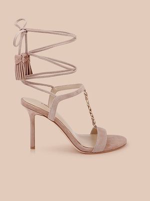 La sandale Bond Suede en rose blush présente un talon à lanières, un lien fin à la cheville, une bride en T à chaîne dorée et un pompon, le tout sur fond de pêche claire.