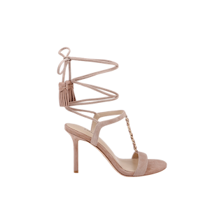 The Bond Suede Sandal is a nude high-heeled strappy heel made from tan suede, featuring an ankle wrap tie, tassel details, and a gold chain accent across the foot, shown on a white background.