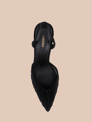 يظهر حذاء «Bowery Mesh Slingback Pump» أسود اللون، ذو مقدمة مدببة وتفاصيل مكشكشة عند مقدمة الحذاء وحزام رفيع خلفي، في صورة مأخوذة من الأعلى على خلفية بيج. ويحمل النعل الداخلي كلمة «LAGENCE» بحروف ذهبية.