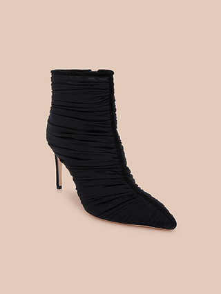 The Fulton Mesh Bootie is a black stiletto bootie with a pointed toe and ruched fabric detail, shown on a beige background.