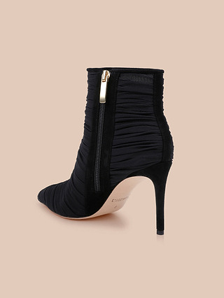 The Fulton Mesh Bootie features a black stiletto heel, pointed toe, ruched mesh texture, and a gold side zipper, showcased against a beige background.