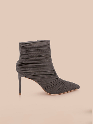 The Fulton Mesh Bootie is a single black stiletto bootie featuring a sleek mesh upper, ruched fabric texture, pointed toe, and thin stiletto heel, displayed against a pale beige background.