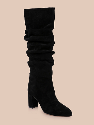 The Fletcher Boot, a black slouchy suede knee-high boot with a block heel, is displayed on a beige background.