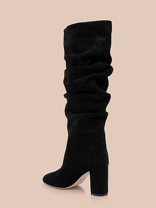 A single Fletcher Boot in black suede, featuring a slouchy knee-high shaft and chunky block heel, displayed against a plain beige background.