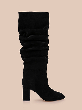 The Fletcher Boot is a black knee-high slouchy suede boot featuring a rounded toe and a high block heel, shown against a plain beige background.