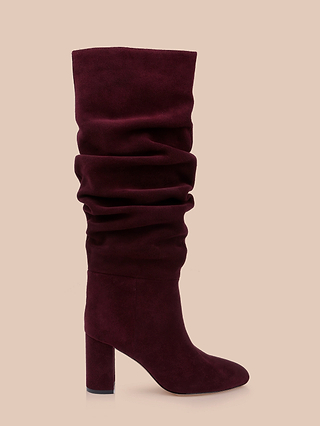The Fletcher Boot—a single burgundy slouchy suede boot featuring a knee-high shaft and a high, block heel—is displayed against a plain beige background, offering the perfect touch of bohemian chic for any outfit.