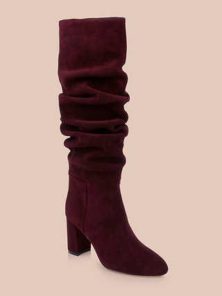 The Fletcher Boot, a single maroon slouchy suede design featuring a knee-high shaft and chunky block heel, is displayed against a plain beige background and captures an effortlessly bohemian chic style.