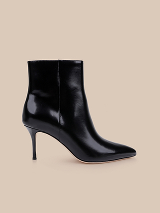 The Houston Bootie is a black leather ankle bootie featuring a pointed toe and a high stiletto heel, showcased against a plain beige background.