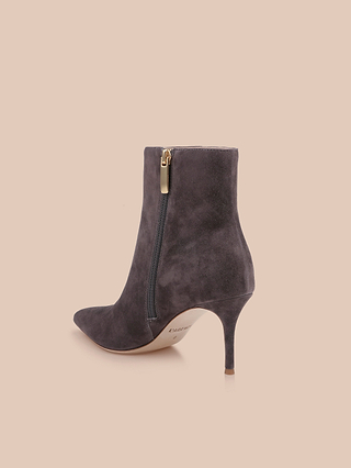 The Houston Bootie, crafted in dark gray suede, features a pointed toe, slim high heel, and elegant side zipper with a gold pull, displayed against a light peach background.