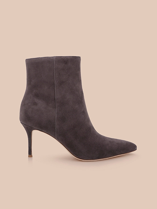 The Houston Bootie, a dark gray suede ankle boot with a pointed toe and thin high heel, is displayed in profile on a light beige background.