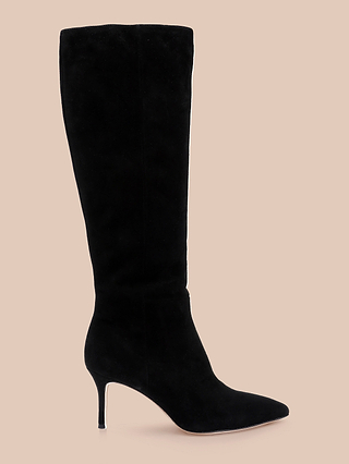 The Herald Boot: a black suede knee-high boot featuring a pointed toe and a slim stiletto heel, displayed in profile against a beige background.