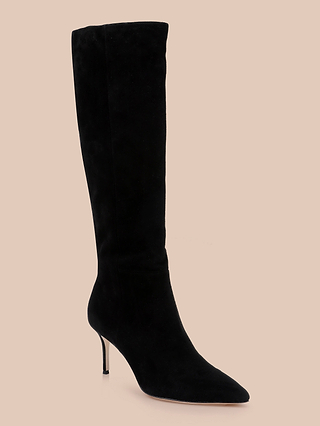 The Herald Boot, a black suede knee-high design featuring a pointed toe and slender stiletto heel, is displayed on a beige background.