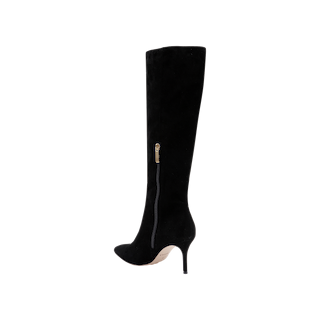 The Herald Boot, a black suede knee-high style featuring a pointed toe, stiletto heel, and a gold side zipper, is photographed against a plain white background.