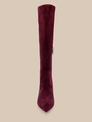 The Herald Boot is a single burgundy suede knee-high boot with a pointed toe and stiletto heel, shown from the front against a plain beige background.