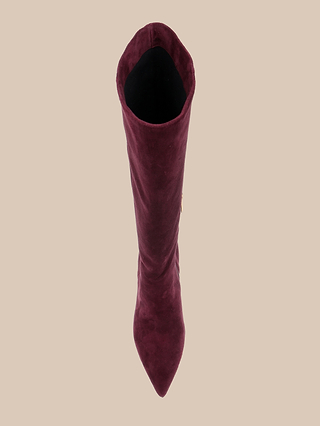 A top-down view of a single Herald Boot featuring a tall, pointed toe stiletto design in maroon suede, set against a beige background.