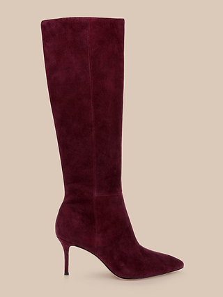 The Herald Boot, a single knee-high boot in burgundy suede featuring a pointed toe stiletto and a slim high heel, is displayed against a beige background.