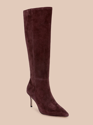 The Herald Boot, a single suede knee-high boot featuring a pointed toe and stiletto heel in dark burgundy reminiscent of elegant mahogany brown, is displayed against a beige background.