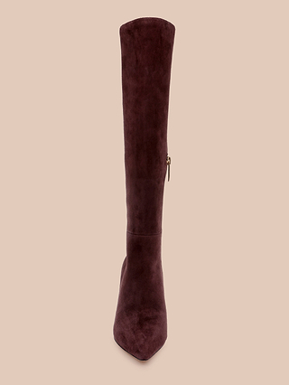 The Herald Boot, a single knee-high, dark brown suede boot featuring a pointed toe, stiletto heel, and side zipper, is displayed front-facing against a plain beige background.