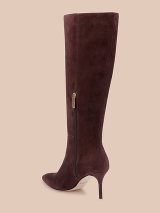 The Herald Boot—a single tall heeled boot crafted from rich mahogany brown suede, featuring a pointed toe, side zipper, and slim stiletto heel—is displayed against a plain light beige background.