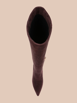 A top-down view of a single Herald Boot—a tall, mahogany brown suede knee-high boot with a pointed toe and elegant stiletto heel—displayed against a plain beige background.