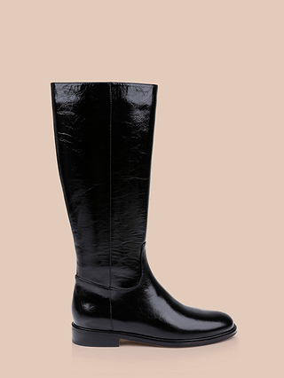 A single Cortland Boot, tall and crafted from shiny black patent leather with a flat sole, is displayed against a light beige background.