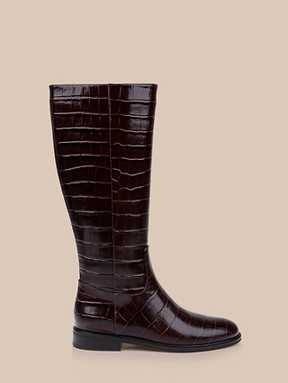 The Cortland Boot is a tall, knee-high design in dark brown croc-embossed leather with a low heel, displayed in profile against a beige background.