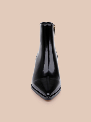 A shiny black leather Vesey Bootie with a pointed toe, viewed from the front against a beige background. A side zipper is visible on the right side of this chic pointed toe bootie.