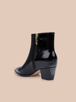 Introducing the Vesey Bootie: a black leather ankle boot featuring a mid heel, side zipper, and pointed toe, stylishly showcased against a plain beige background.