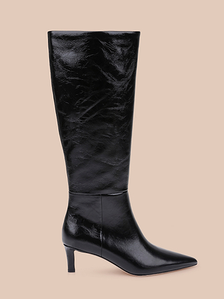 The Baxter Boot, a single black knee-high leather boot featuring a pointed toe and low heel, is displayed on a beige background for a comfortable yet stylish look.