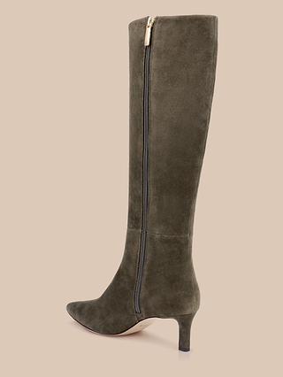 The Baxter Boot, a knee-high design in ash olive green suede with a pointed toe, mid-height heel, and side zipper, is showcased against a beige background for a distinctly stylish look.