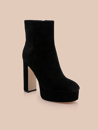The Soho Bootie, featuring black suede with a high platform block heel and rounded toe, is displayed on a beige background.