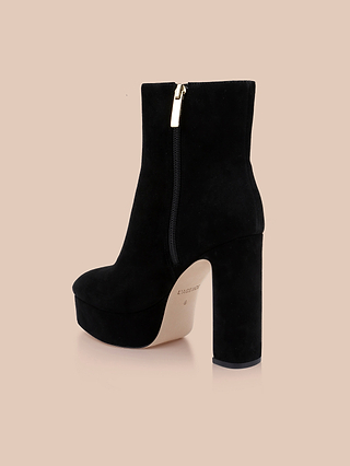 The Soho Bootie is a black suede platform ankle boot featuring a chunky block heel and side zipper, displayed against a light beige background.