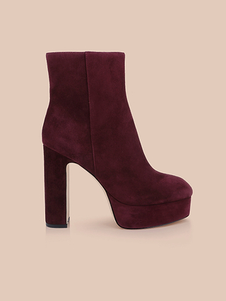 The Soho Bootie—a single burgundy suede shoe featuring a high chunky block heel and platform sole—is shown in profile against a plain beige background.