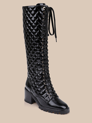 Tribeca Boot: A black, knee-high lace-up combat boot featuring a quilted, glossy patent leather texture, chunky block heel, and lugged sole, displayed against a plain beige background.